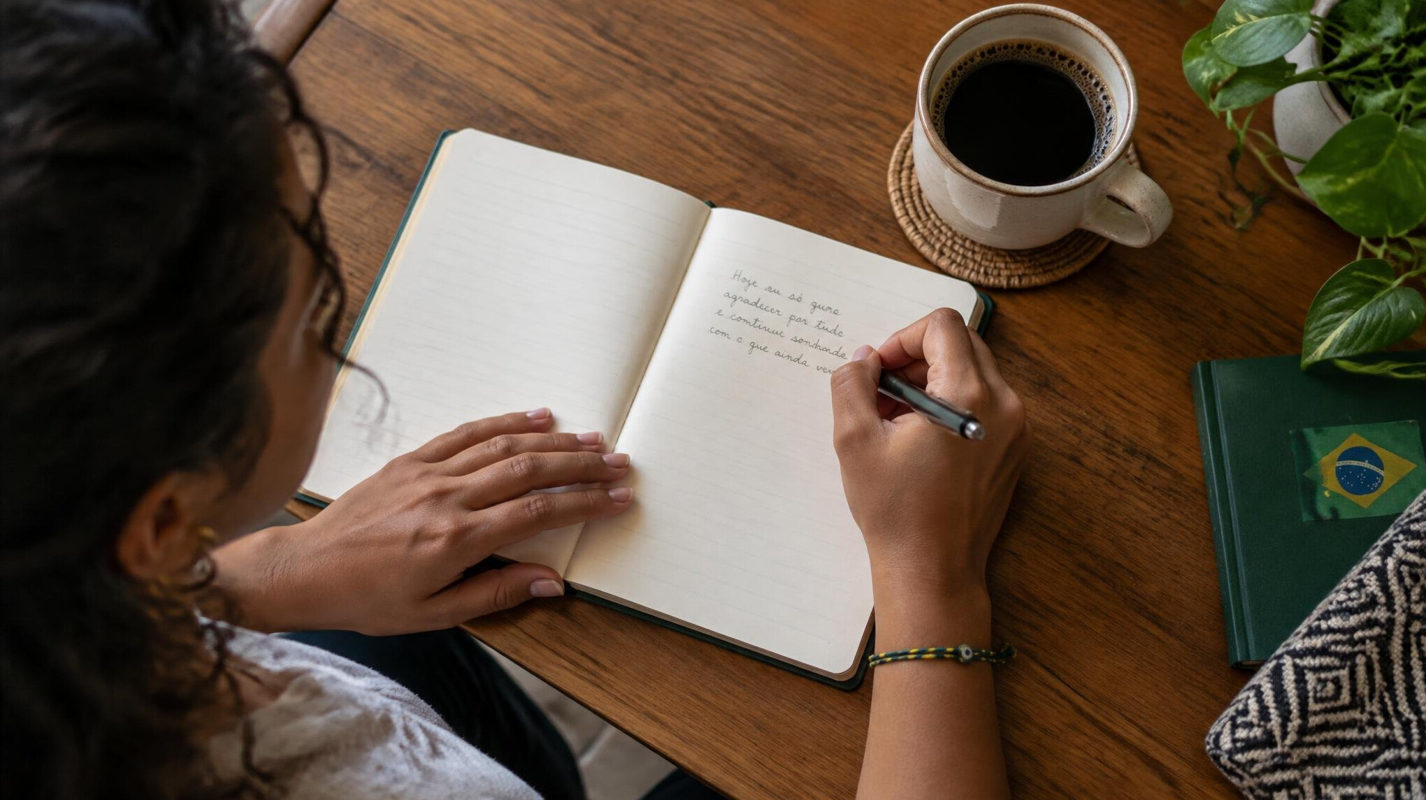 Person writing thoughtfully in a journal at a wooden desk